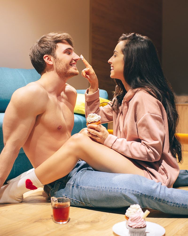 Un couple assis par terre, elle lui touche le nez en riant